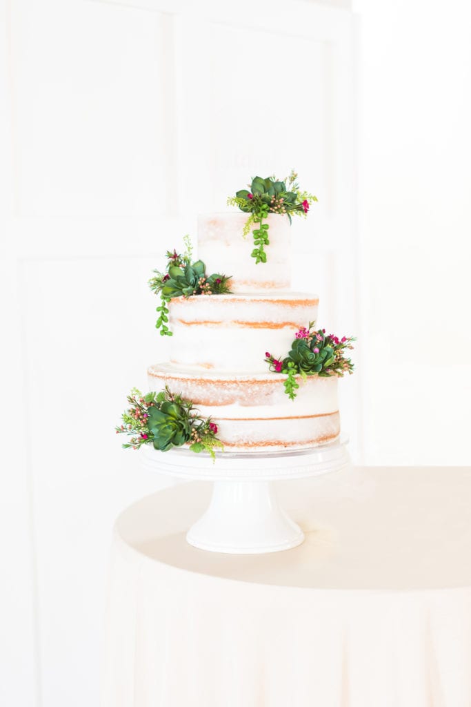 A naked wedding cake adorned with greenery