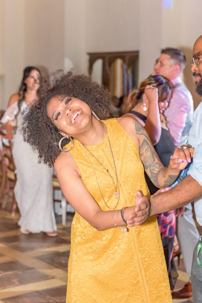 A wedding guest dances, laughing, while the bride dances behind her during the open dancing part of the timeline