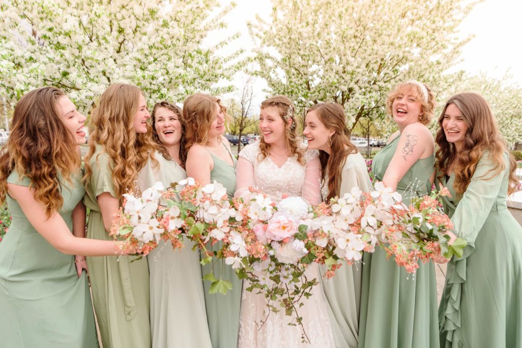 A wedding day pose with bridesmaids smiling and laughing at each other while they hold their bouquets.