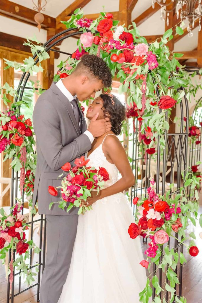 A beautiful bride and groom go in for a kiss, surrounded by a red rose lattice.