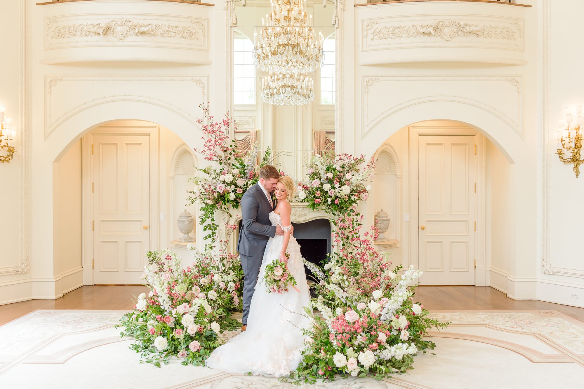 An elegant display of florals is placed all around the fireplace at this mansion wedding.