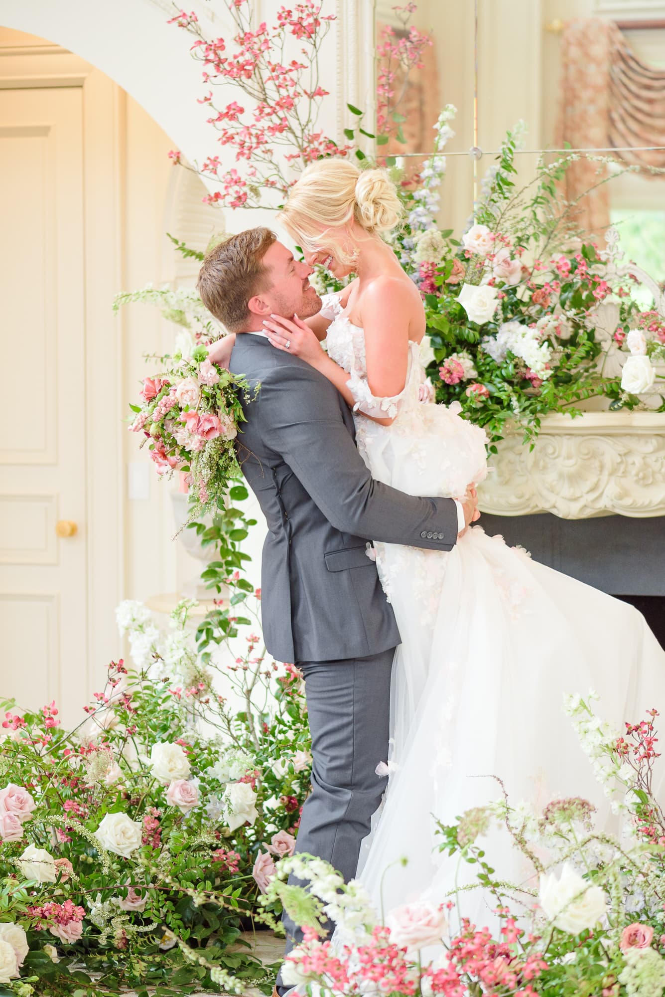 The groom picks his bride up and spins her around in the drawing room of this elegant mansion.