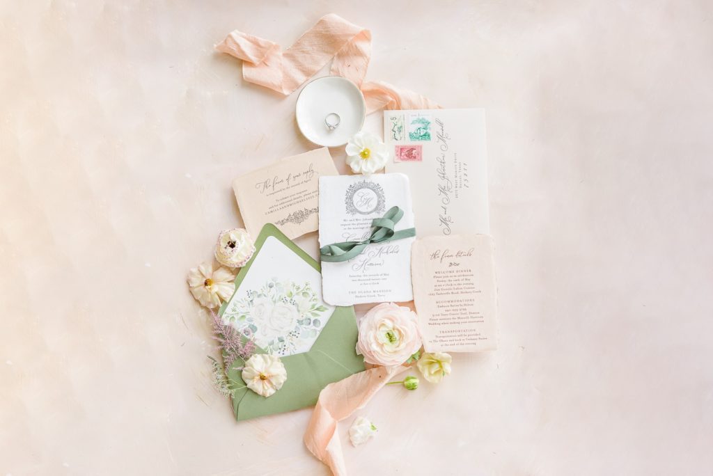 Photos of wedding invites with the envelope, cards, flowers, ribbon, and ring included.