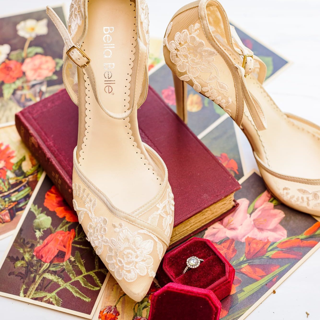 A picture of shoes sitting on top of a book. There's a ring, and lots of flower pictures scattered on the ground.