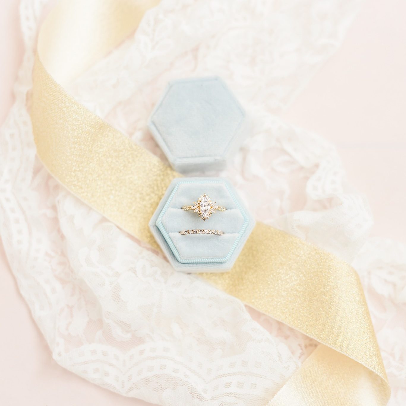 An engagement ring in an open top ring box with ribbons behind it.