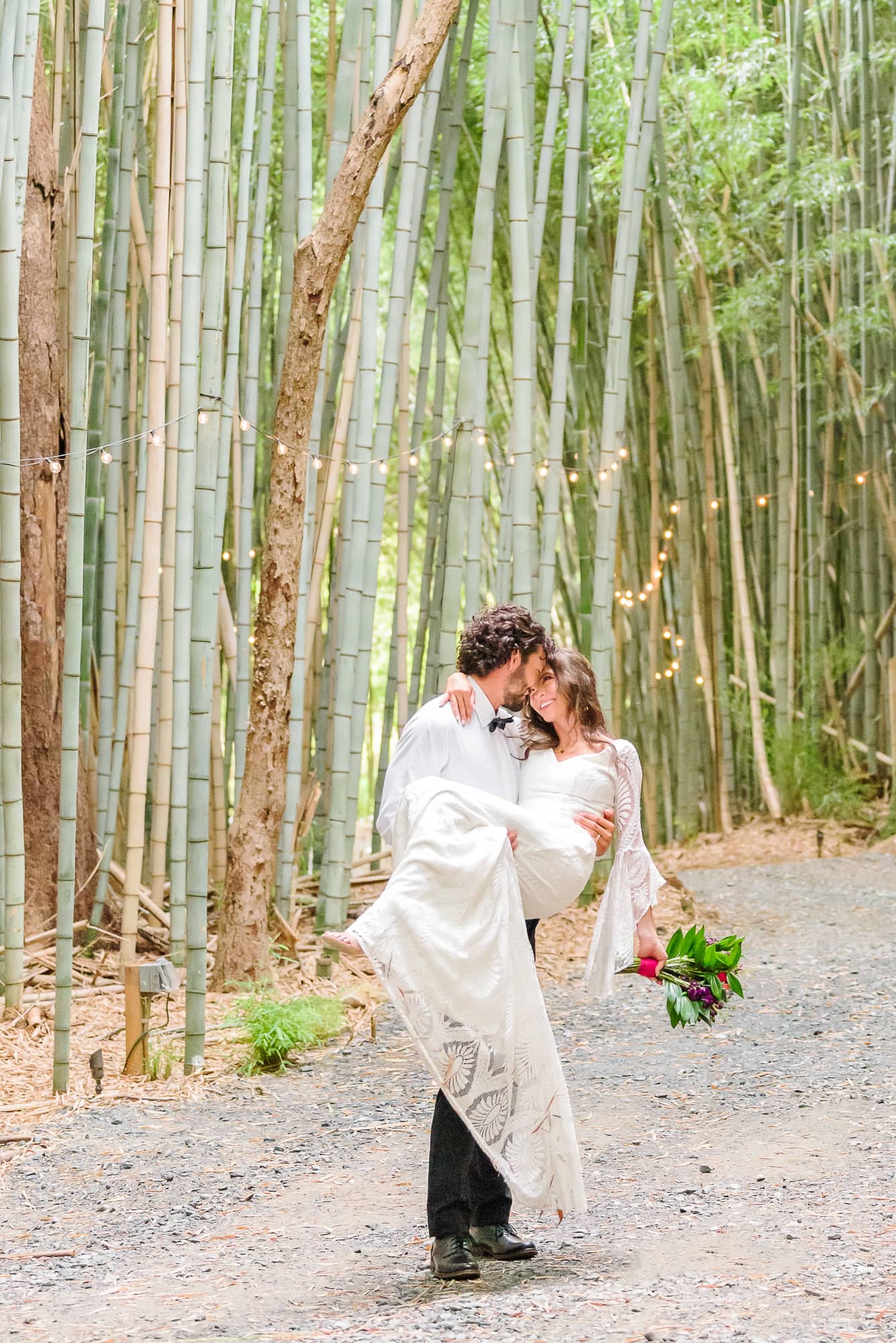 Trevor picks Kaelyn up and carries her through their wedding venue's bamboo forest in Belmont, NC.