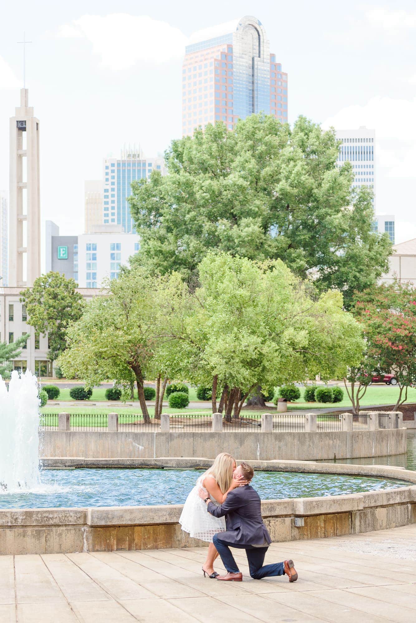 Heather kneels down to kiss Corey after he proposed at Marshall Park in Charlotte.