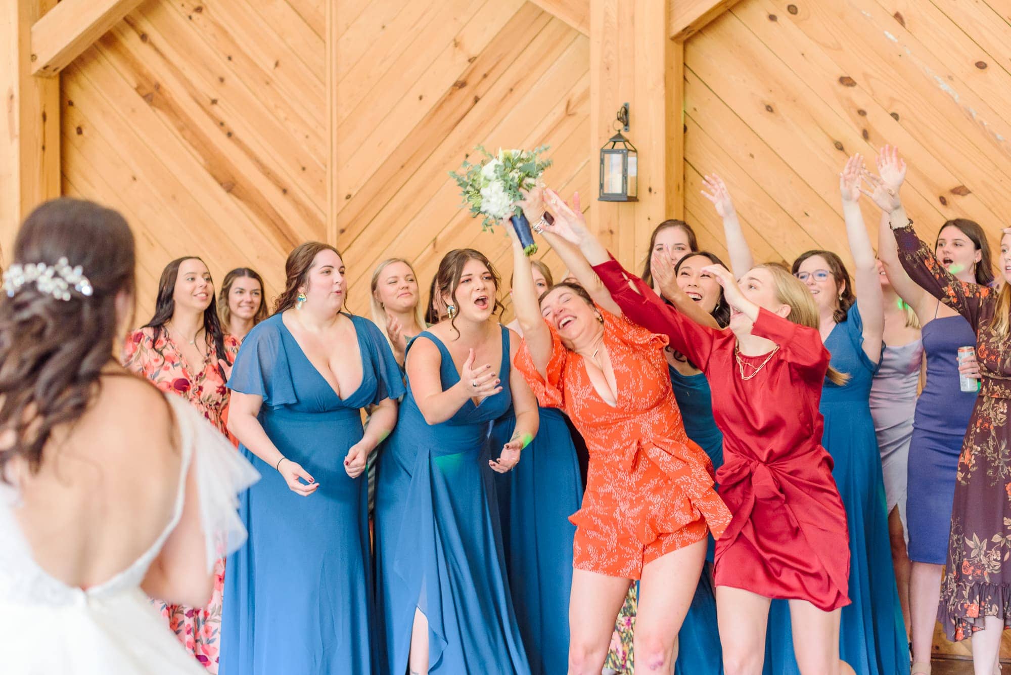 The single ladies jump for a chance to catch Natalie's bouquet inside the Alexander Homestead reception barn.
