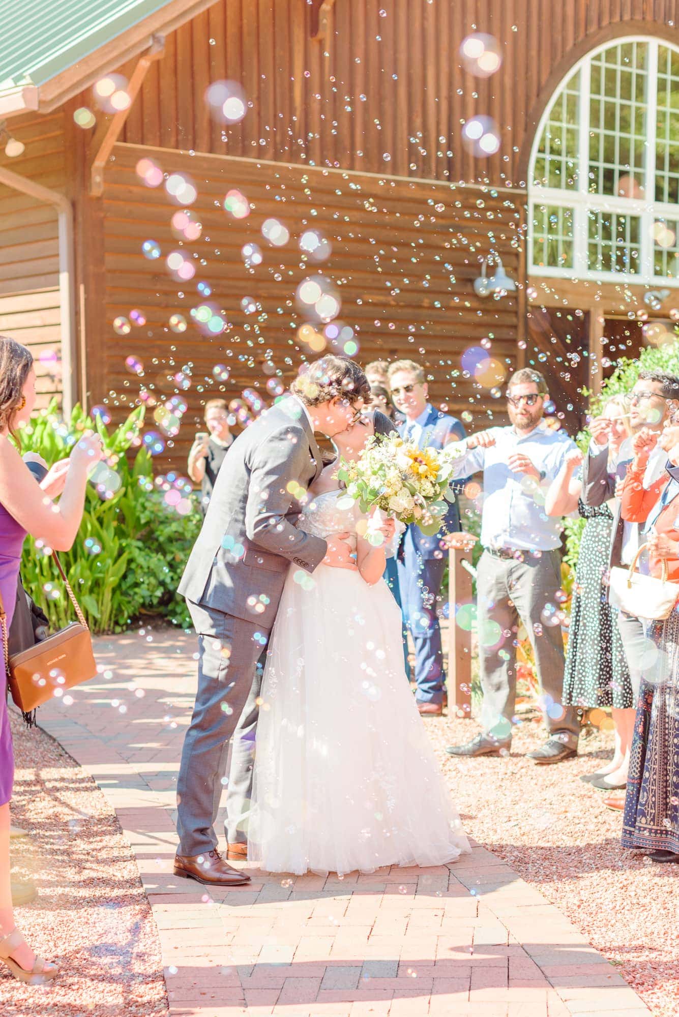 Natalie and Tommy kiss in a swarm of bubbles in front of the barn at Alexander Homestead.