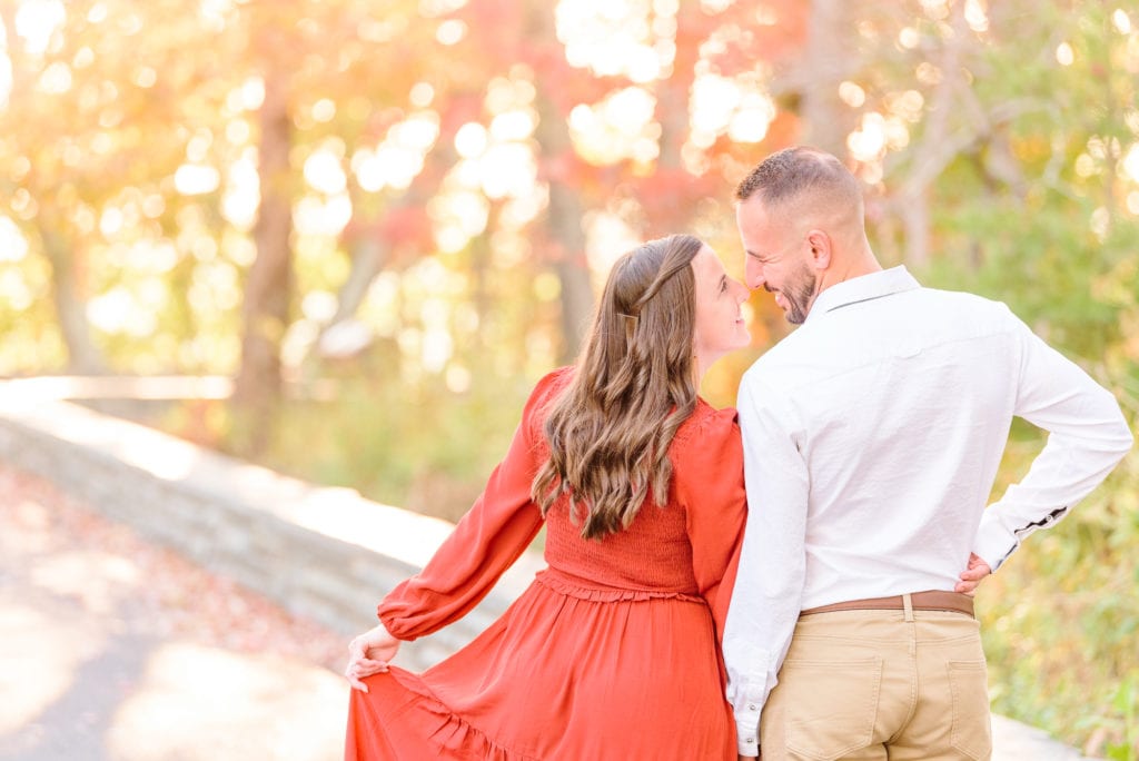 Alicia and Joey hold hands in front of the fall leaves during their engagement session in North Carolina.