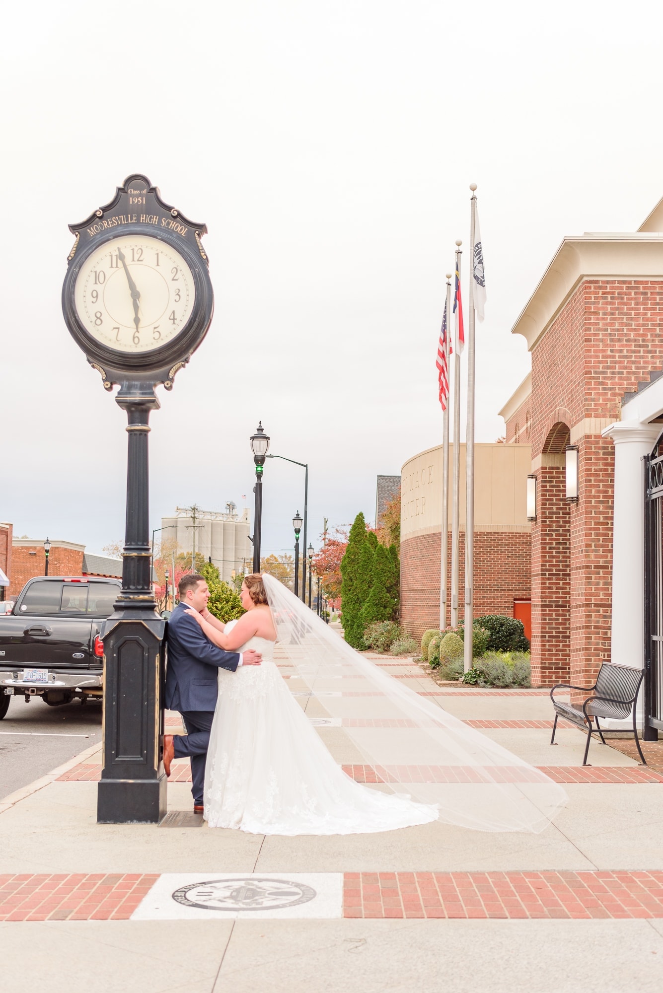 The bride and groom stand next to a striking clock on the street near the Charles Mack Citizen Center.