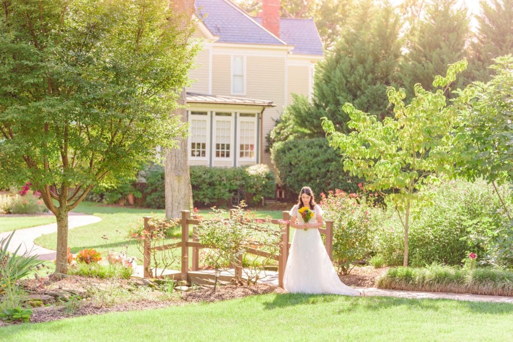 Natalie smells her bouquet of flowers for her bridal photos and you can see the Alexander Homestead house behind her.