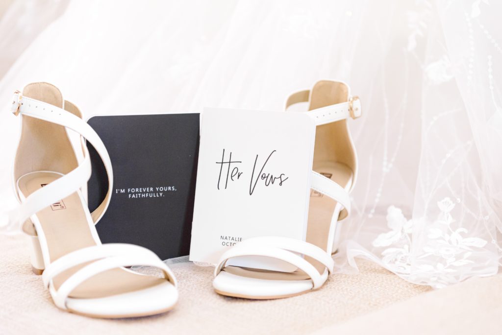 Natalie's shoes sit on the hem of her wedding dress. Her and Tommy's vow booklets are standing on the shoes.