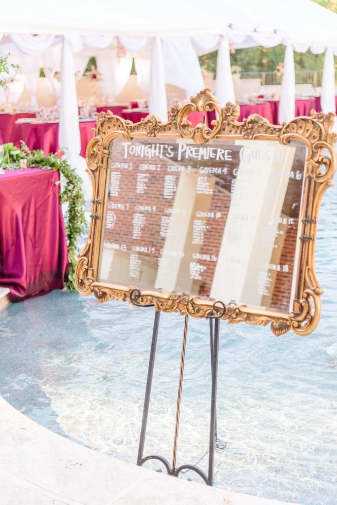 A Hollywood themed wedding seating chart written on an ornate gold mirror.
