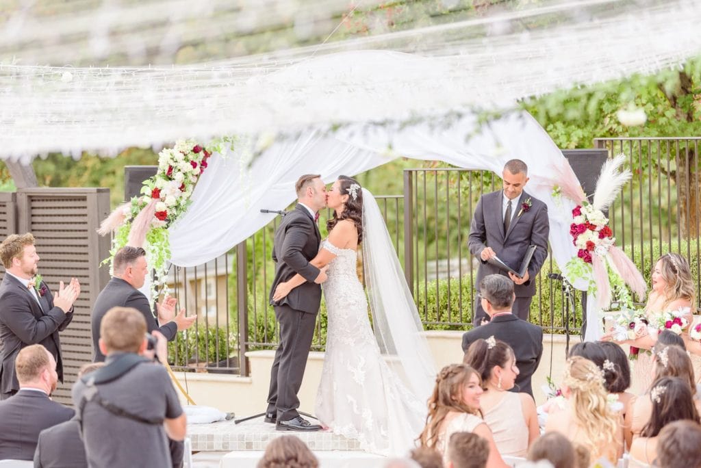 Ashley and Seth share their first kiss at their Hollywood themed wedding as guests stand up and applaud.