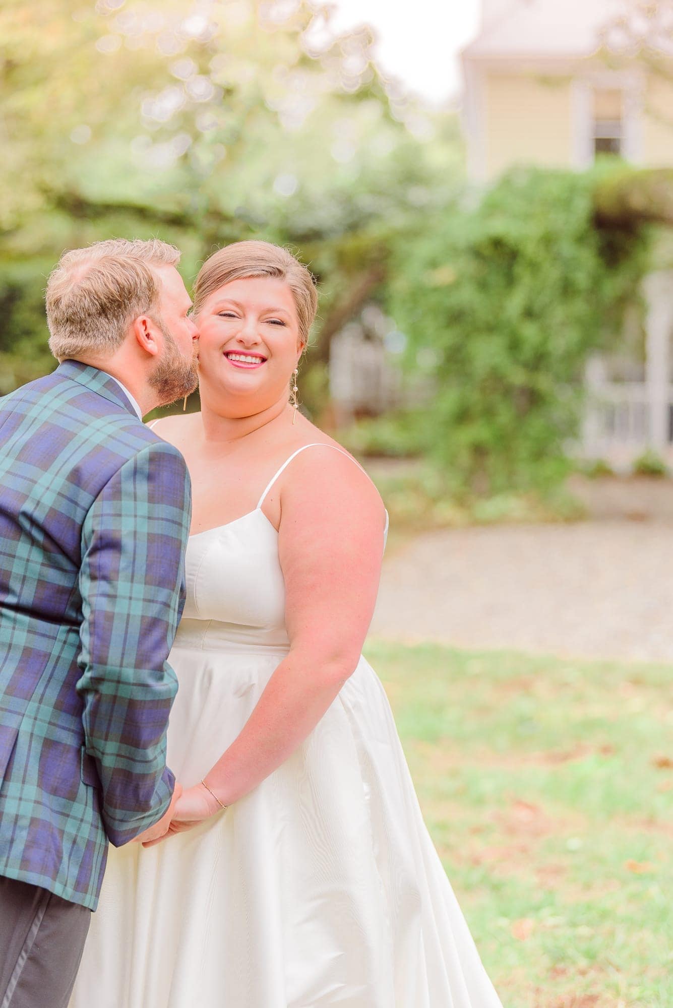 The groom kisses his bride on the cheek as she beams into the camera during their first look at the Whitehead Manor.