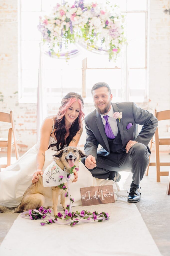 The bride and groom pet their dog on the aisle runner at the Kettle Room wedding venue.