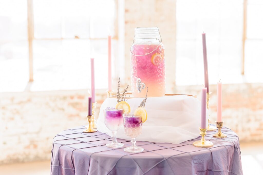 A beautiful drink station is set up in the Kettle Room with pink and purple cocktails in antique glasses.