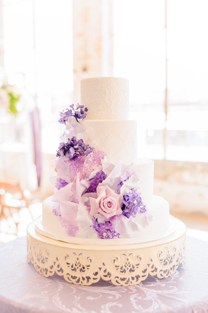 A gorgeous buttercream cake is adorned in purple flowers, the Kettle Room is visible behind it.