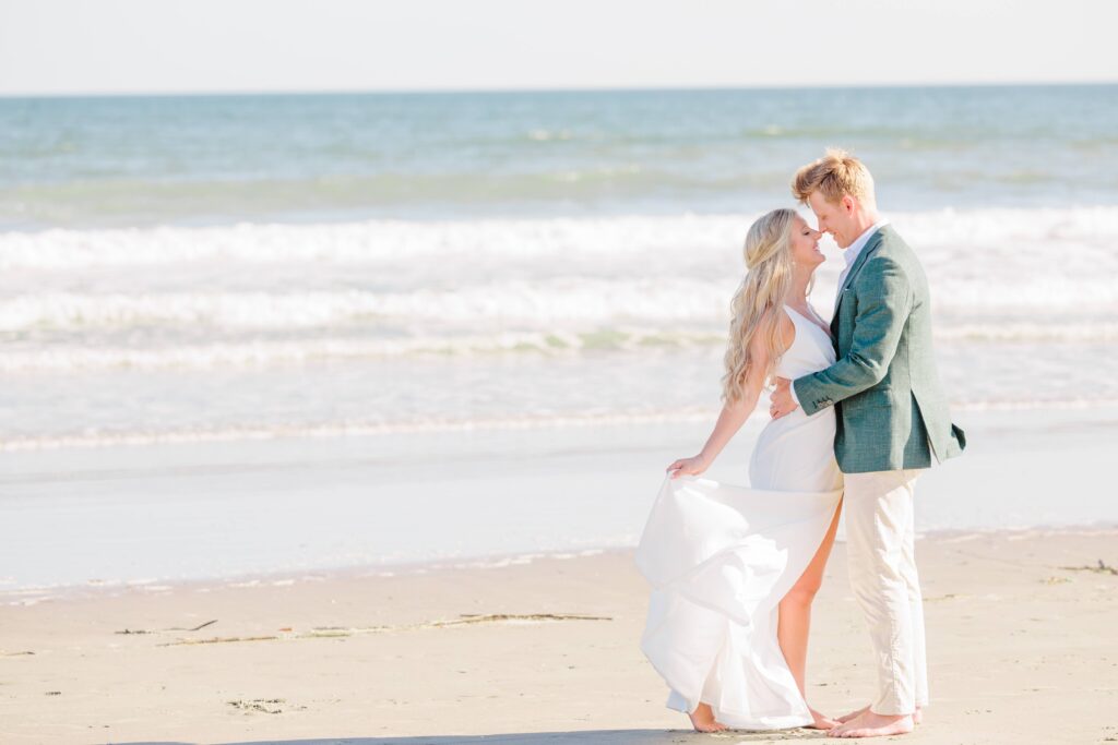 The couple holds each other nose to nose with the ocean water behind them in their beach engagement pictures.