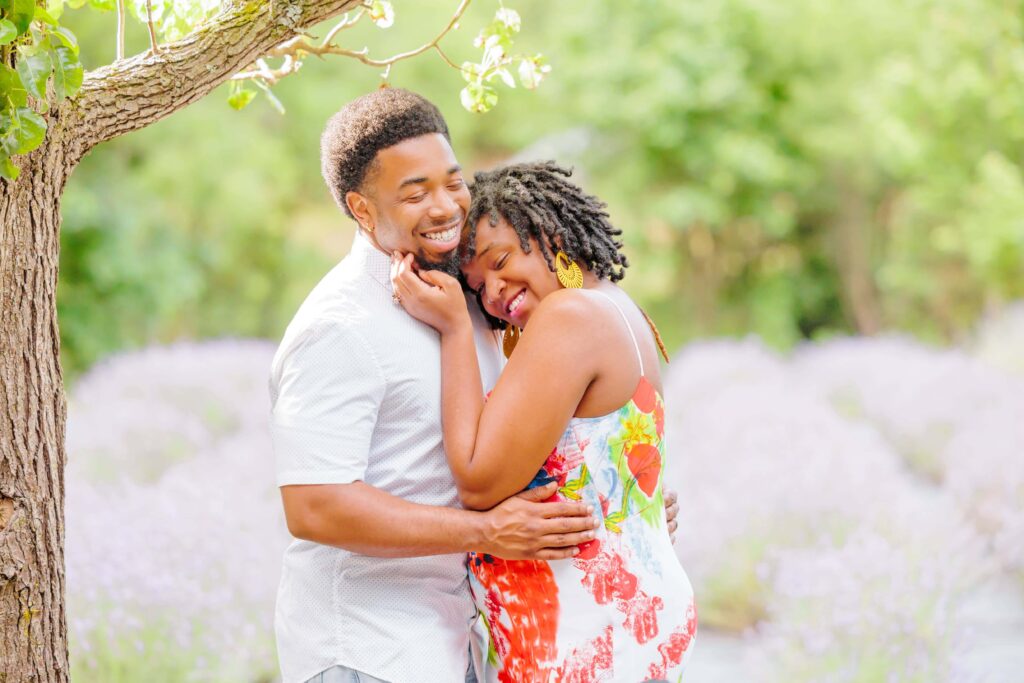 The couple smiles and holds each other in front of the lavender at the Lavender Farm in NC.