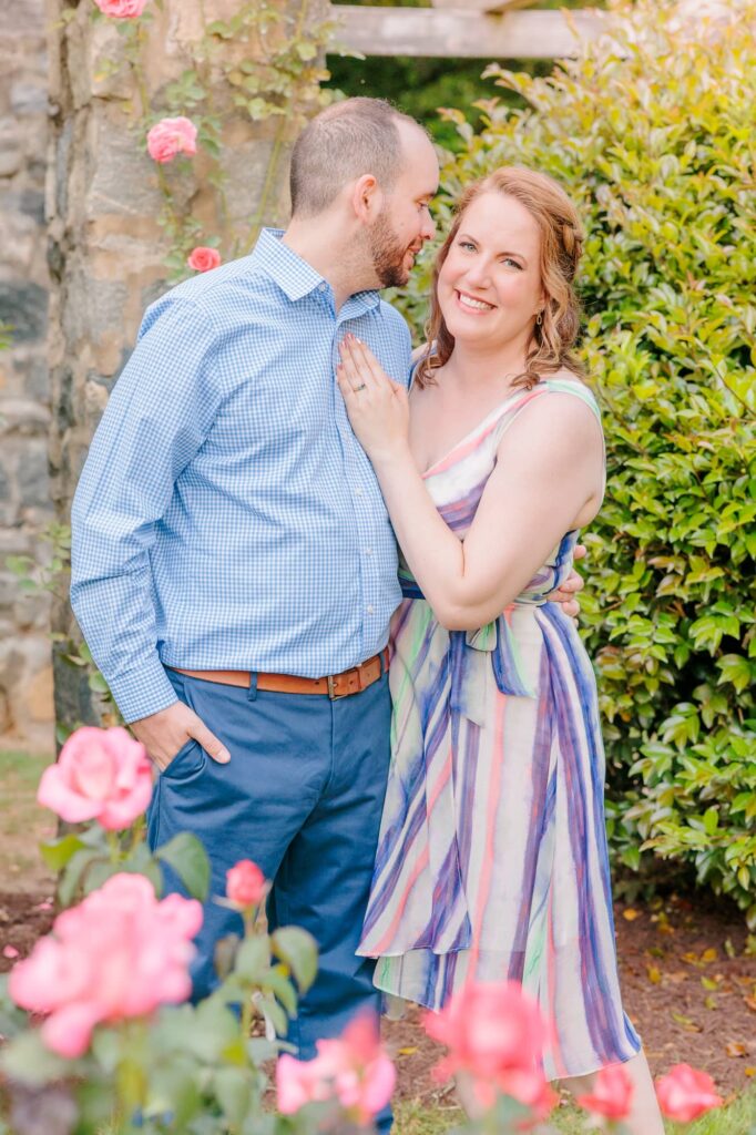 Emelia smiles at the camera as Wakefield looks adoringly at her during their engagement session at the Raleigh rose garden in North Carolina.