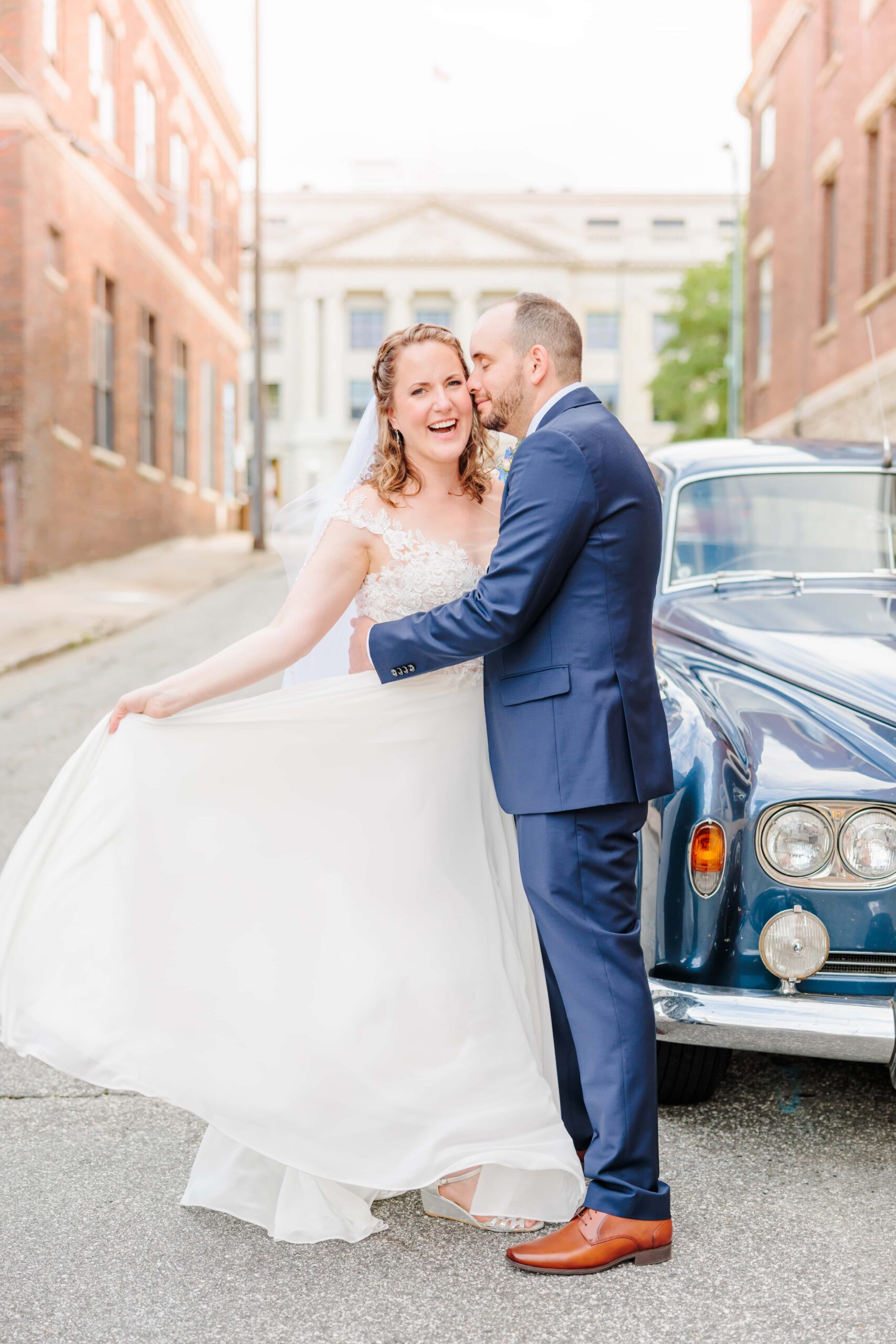 A happy couple stands in the streets of Greensboro, holding each other and smiling at the camera after their wedding.