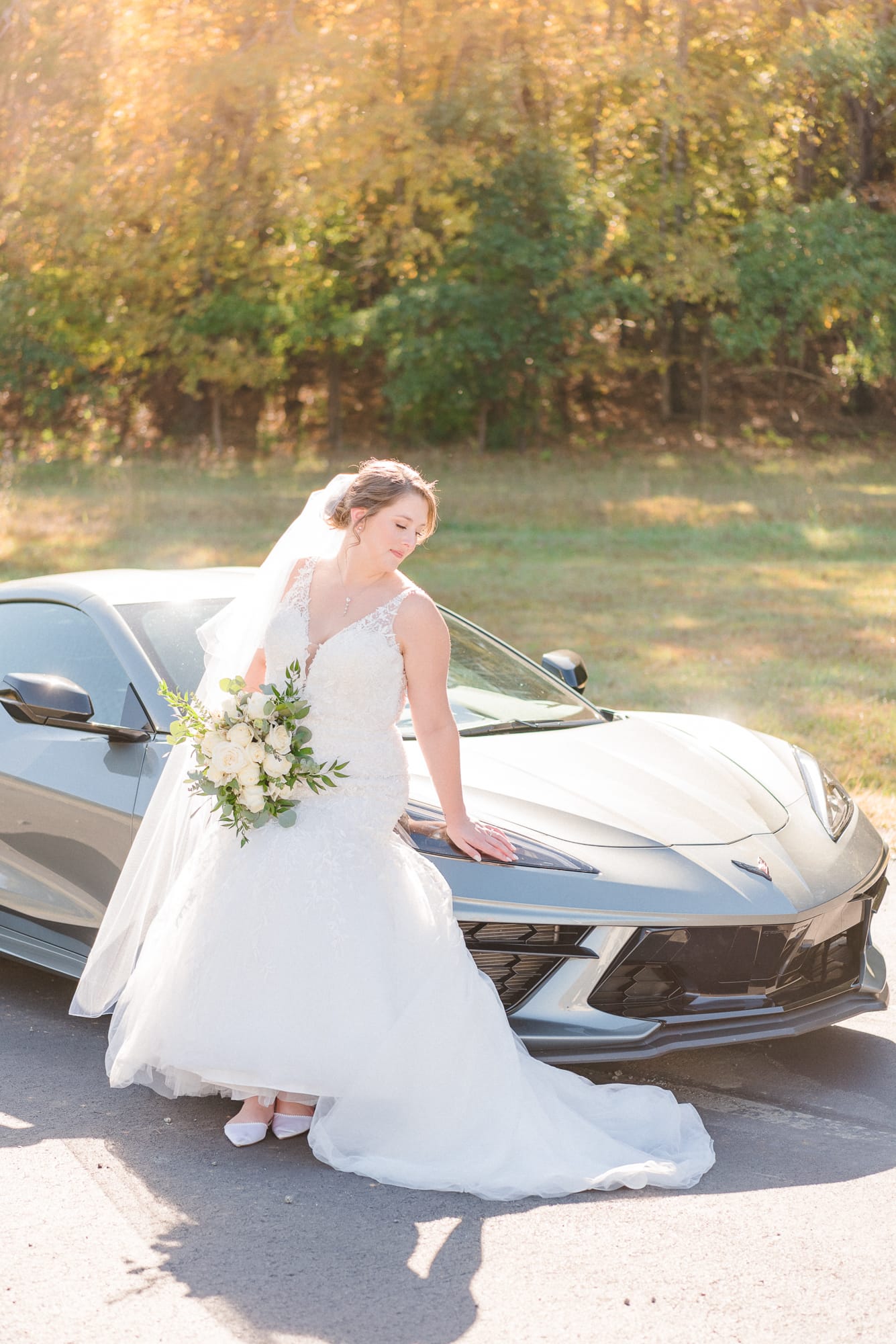 Katelynn stands next to her sleek, grey car in front of the forest at Low Meadows Estate.