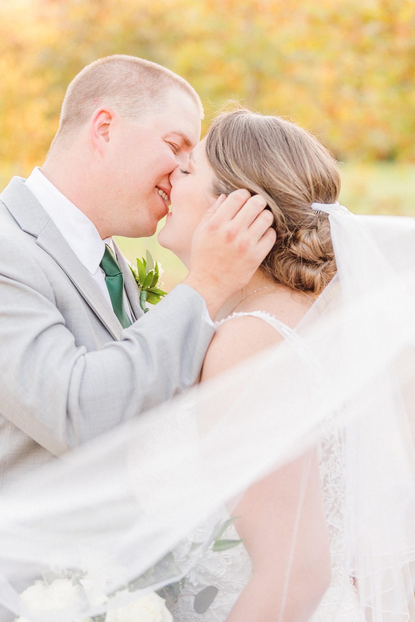 Katelynn and Alec kiss while their veil swirls around them on the grounds of the Low Meadows Estate wedding venue.