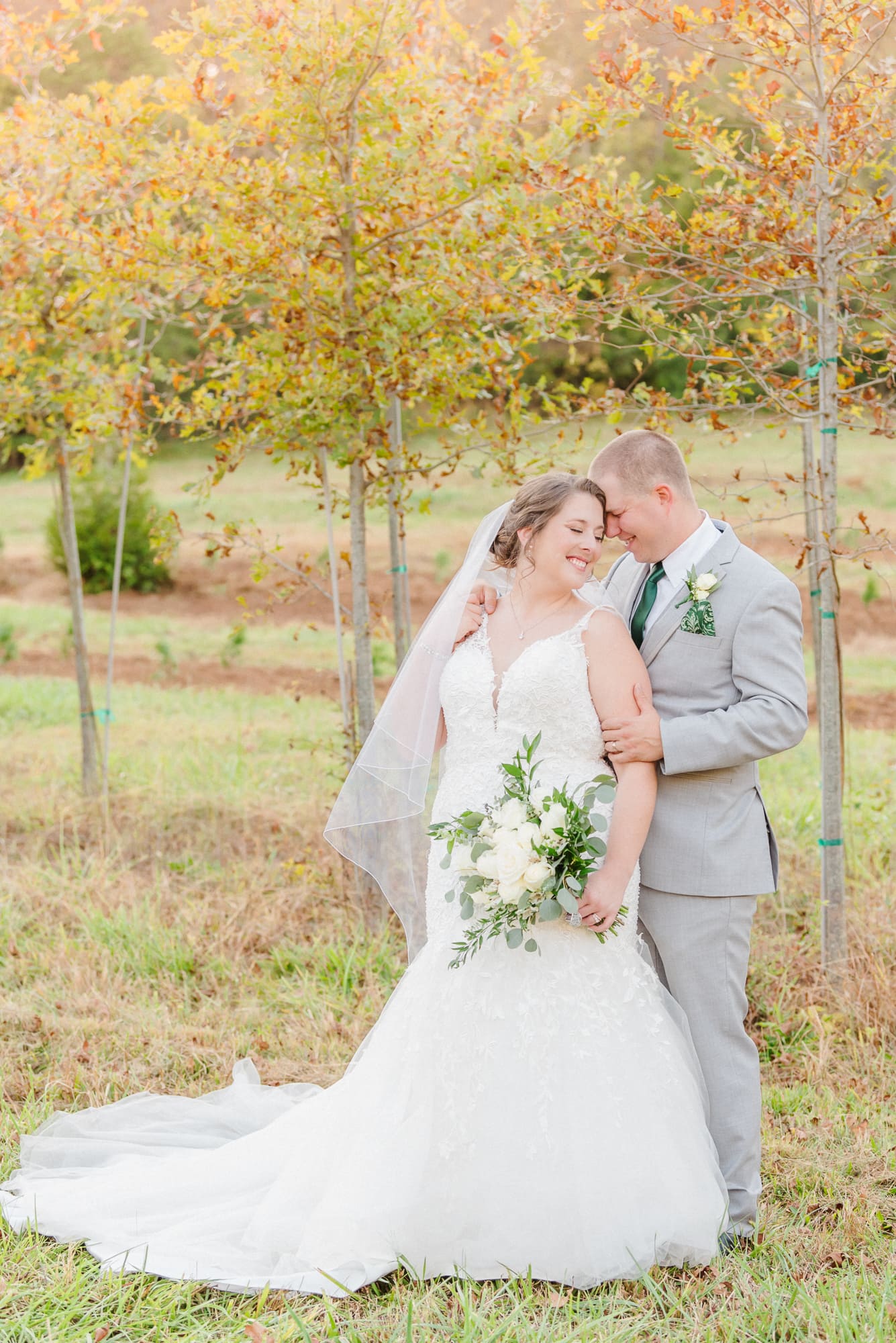 Low Meadows Estate has young trees that change with the fall colors. The bridal couple smiles and holds each other in front of them.