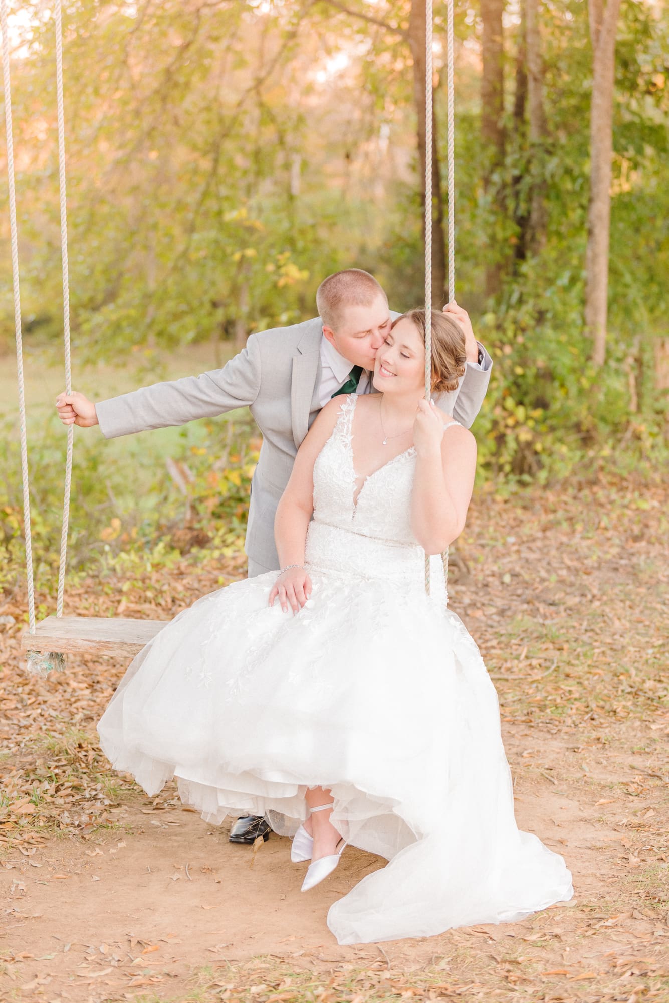 The groom kisses the bride's cheek as they swing on the swinging bench at Low Meadows Estate.