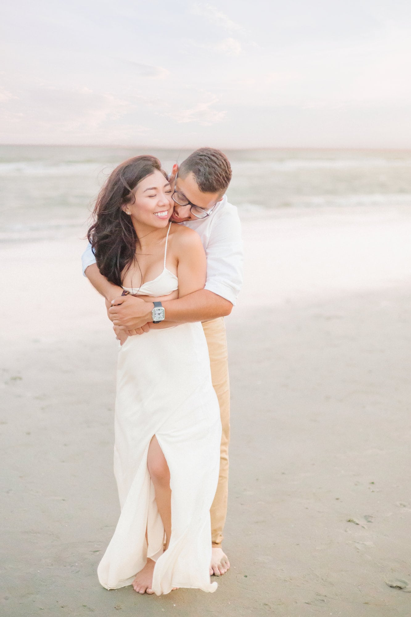 Engagement pictures on the beach wearing a white dress, a white shirt, and khaki pants.