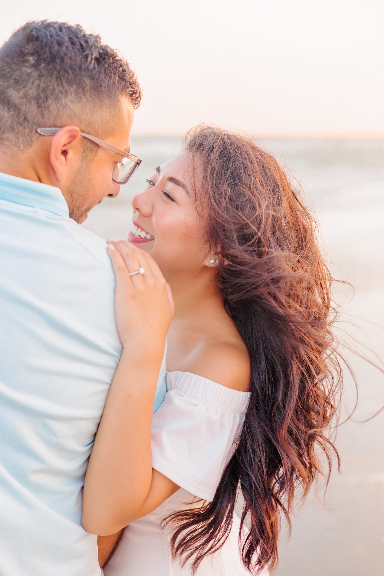 Carisil and Edgar smile at each other, unaware of the camera during their engagement photos on the beach.