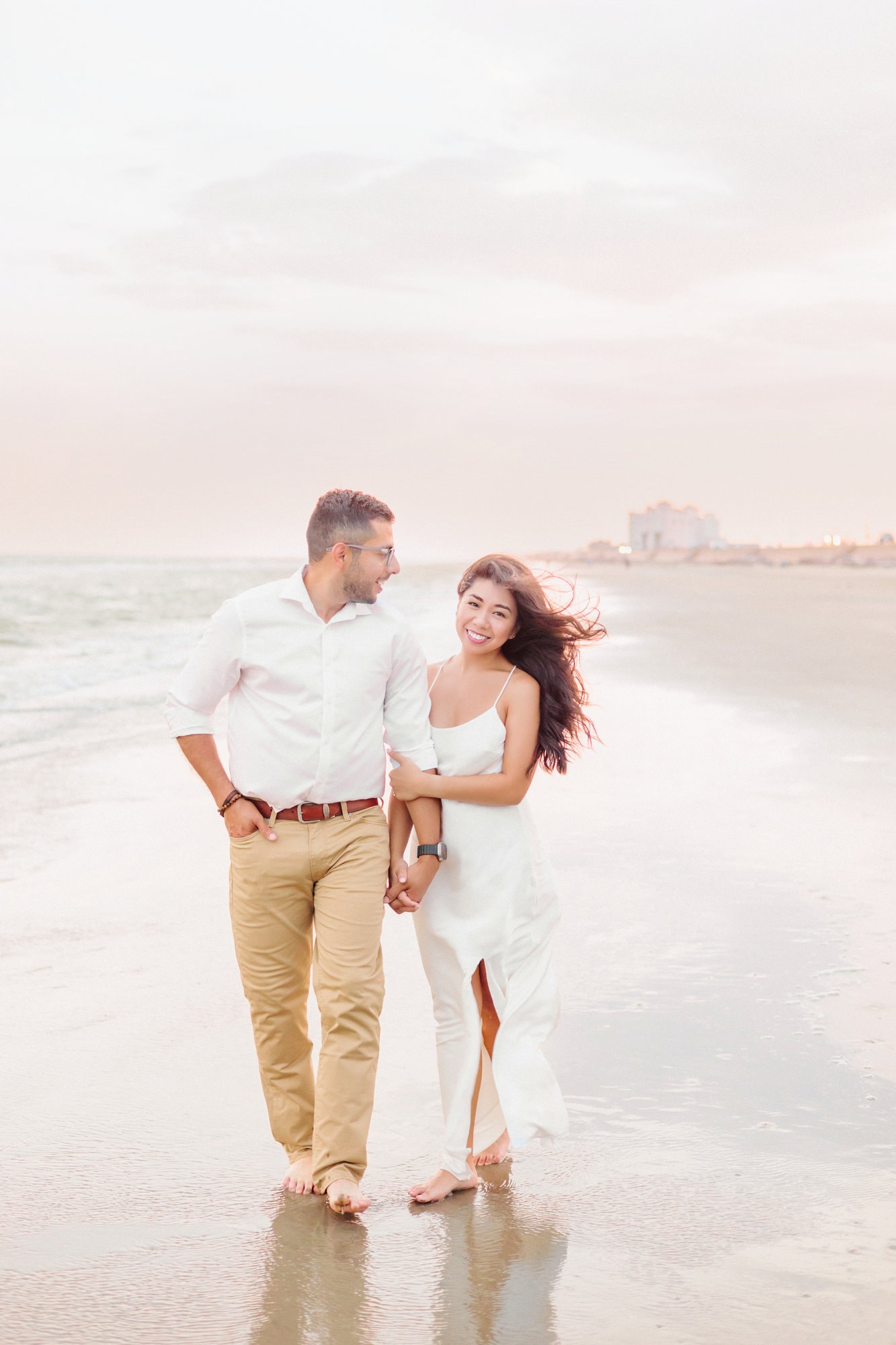Elegant engagement pictures on the beach with the engaged couple walking hand in hand by the water.