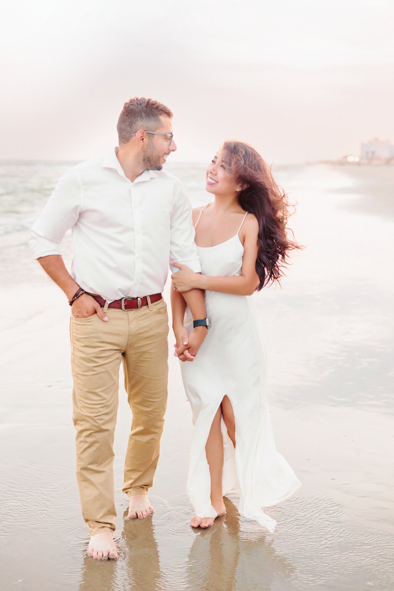 Engagement pictures at the beach with the couple walking hand in hand next to the water.