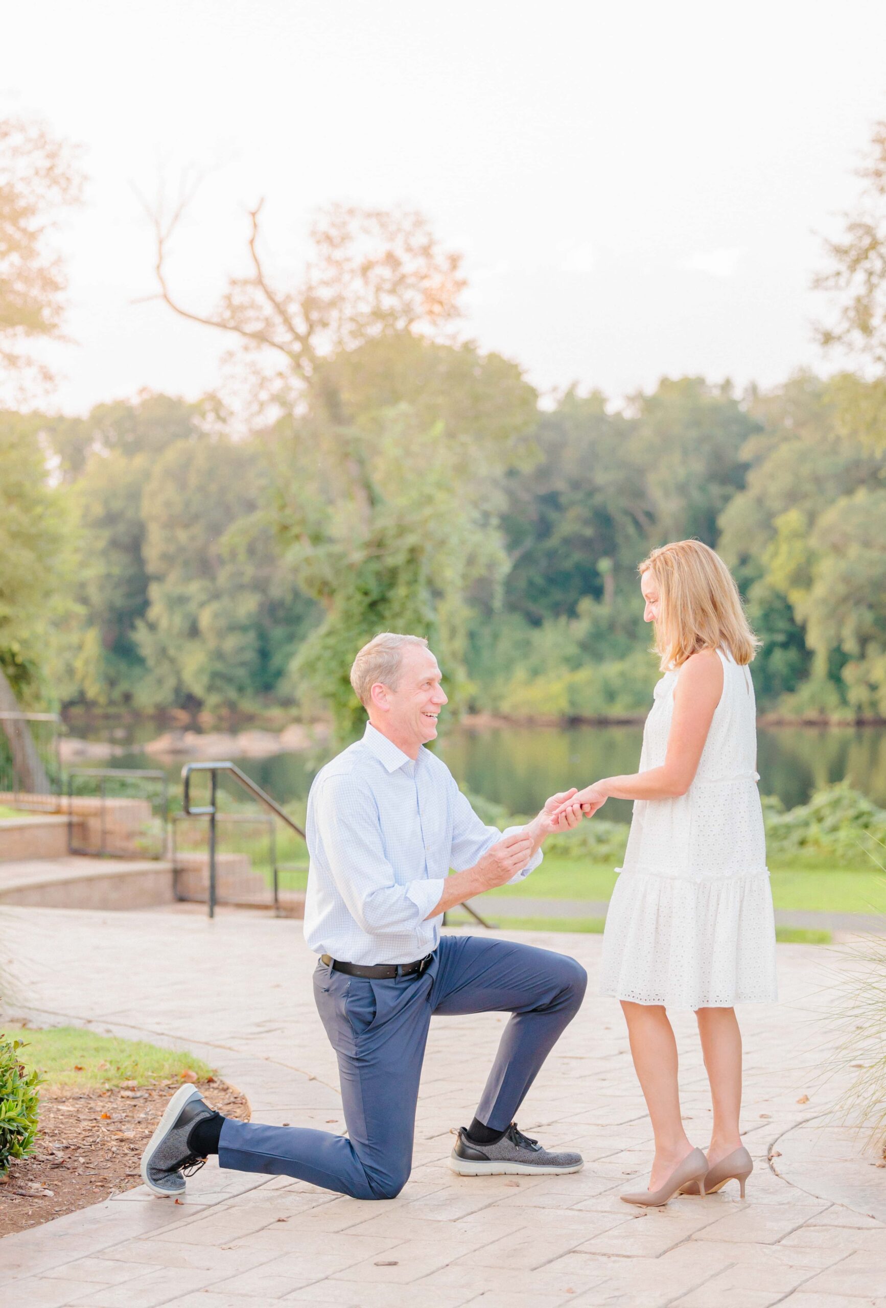 An image of Matt getting down on one knee to propose to Janet in front of the riverwalk in Rock Hill, SC.