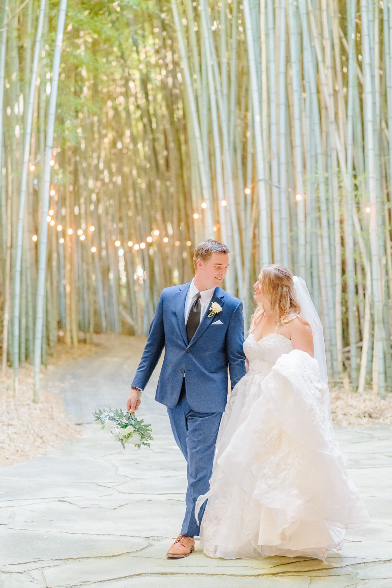 The bride and groom walk through the forest near their barn wedding venue.