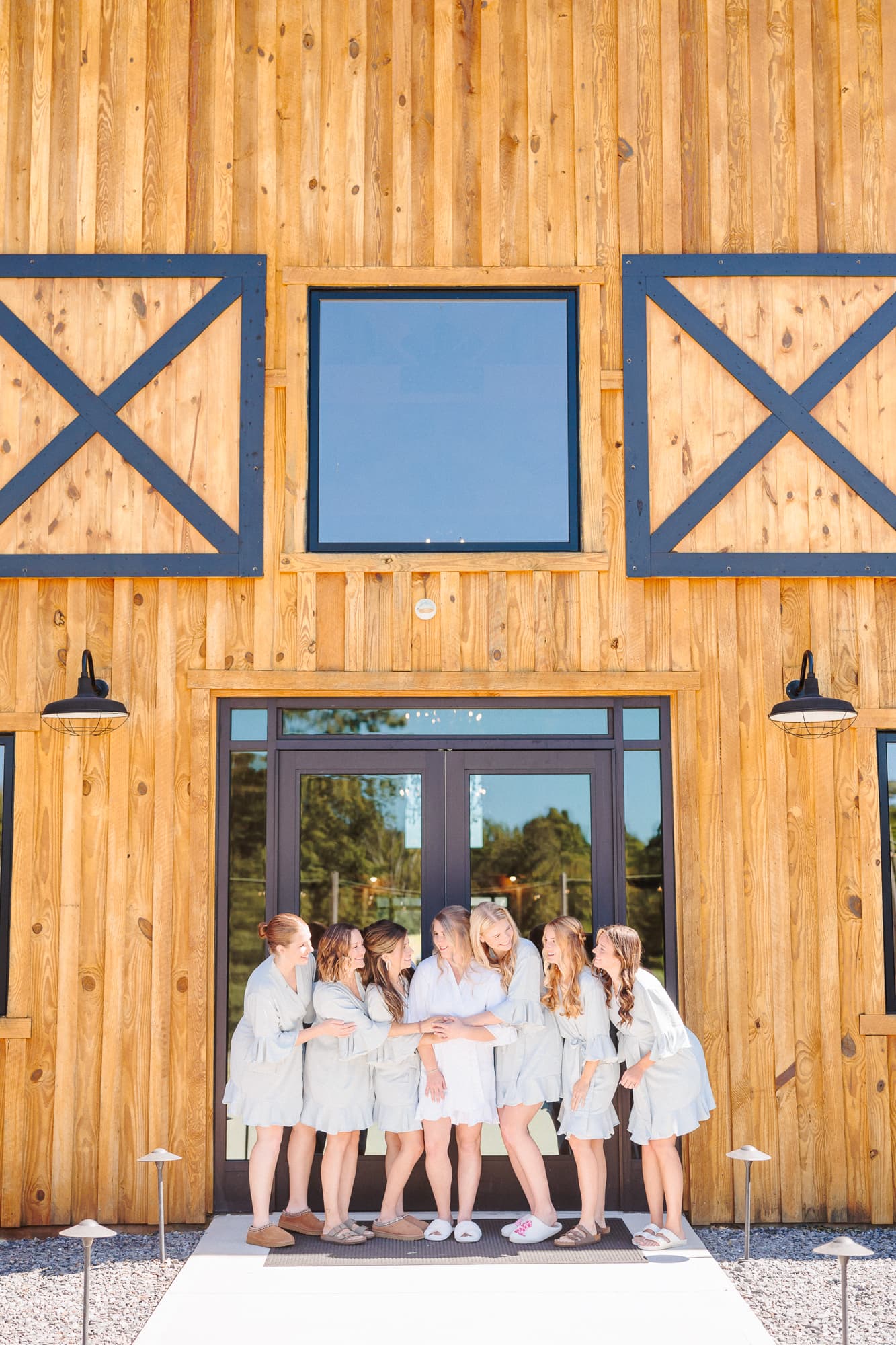 The bride and her bridesmaids stand in front of the barn wedding venue in their matching robes.