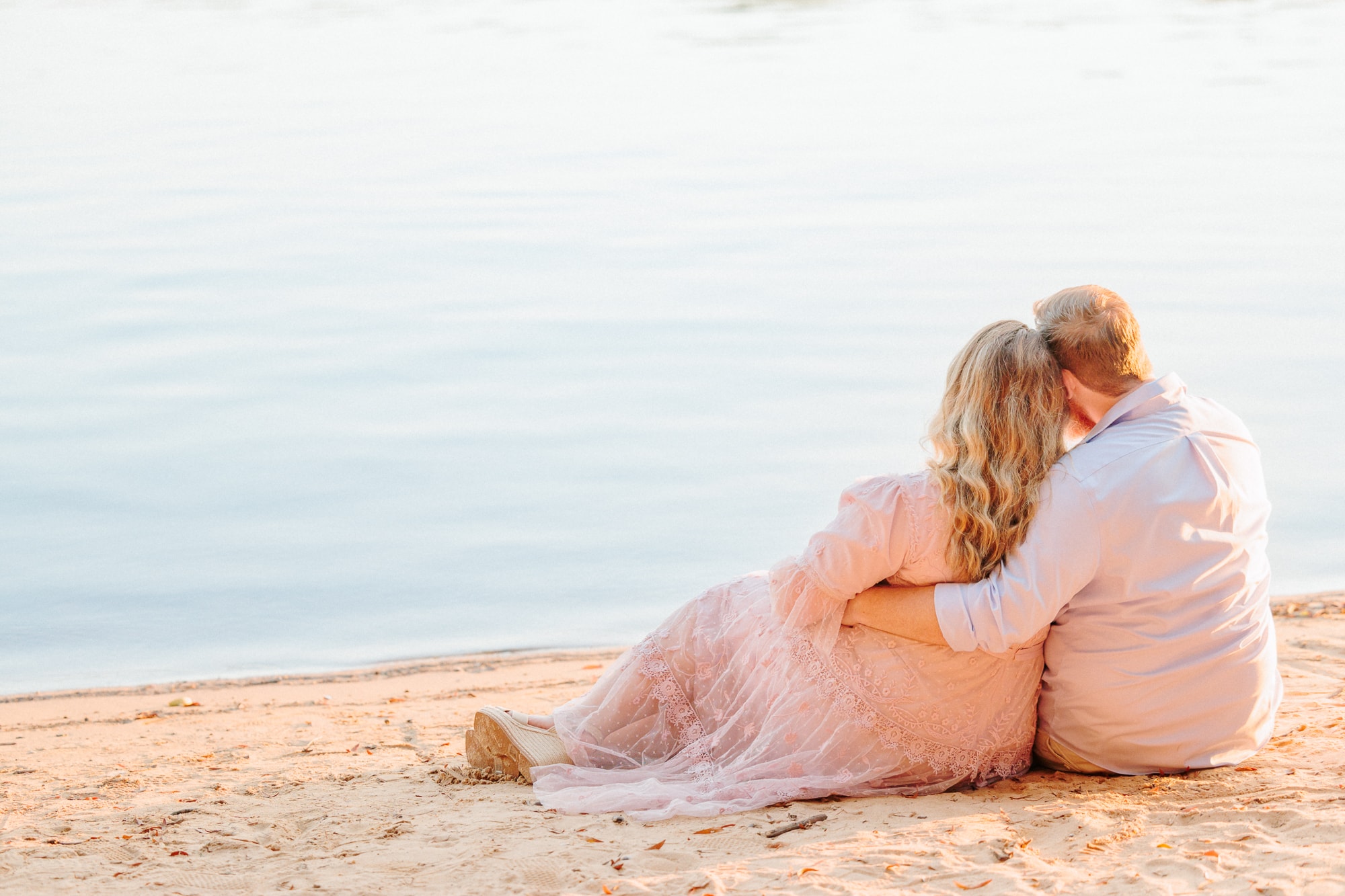 During their Huntersville engagement session, the couple sits on the sandy shores of the lake and looks out at the water.