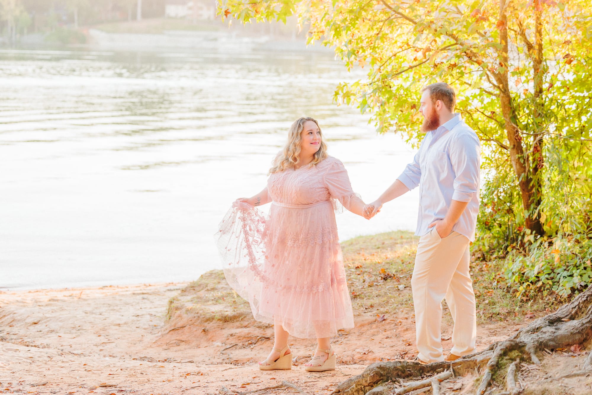 The couple holds hands and walks along the lake for their Huntersville engagement photos.