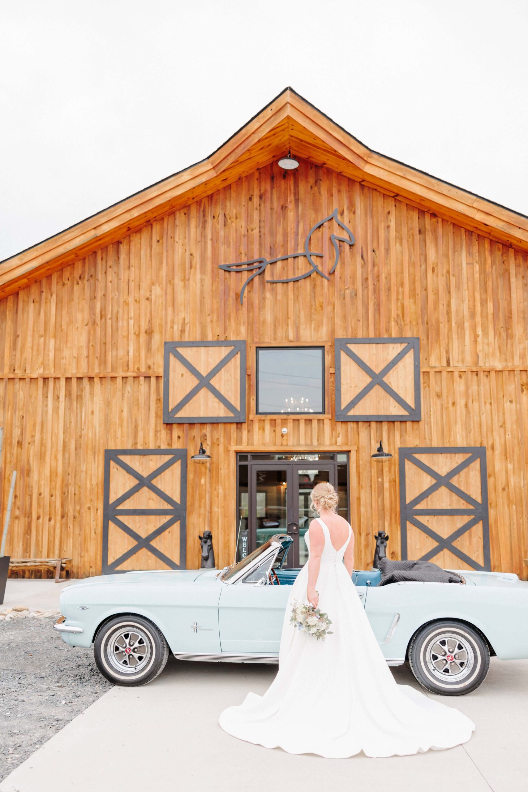 A classic bridal portrait with a vintage car in front of a barn wedding venue.