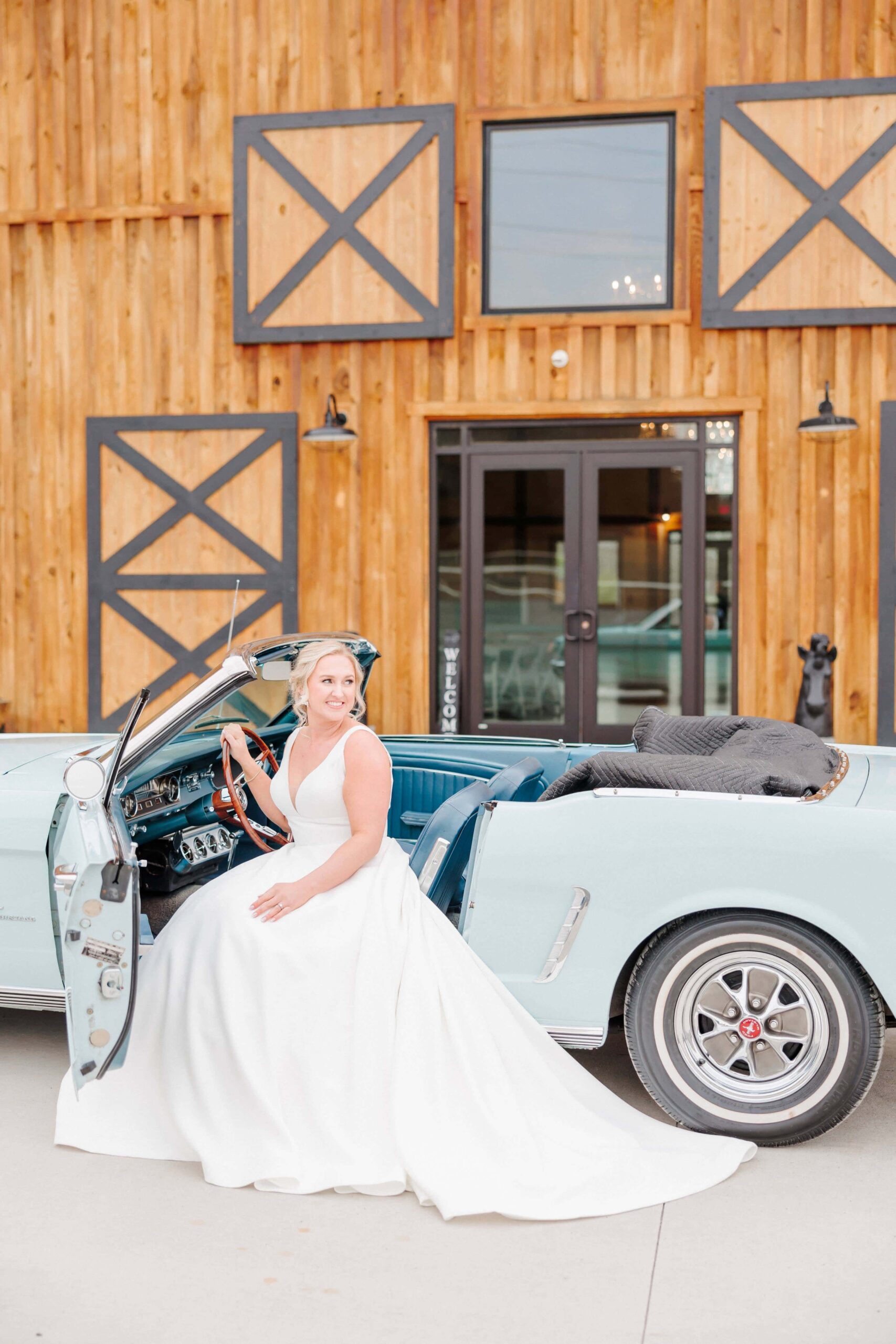 The bride and her classic car are parked in front of the wedding venue entrance for bridal photos.