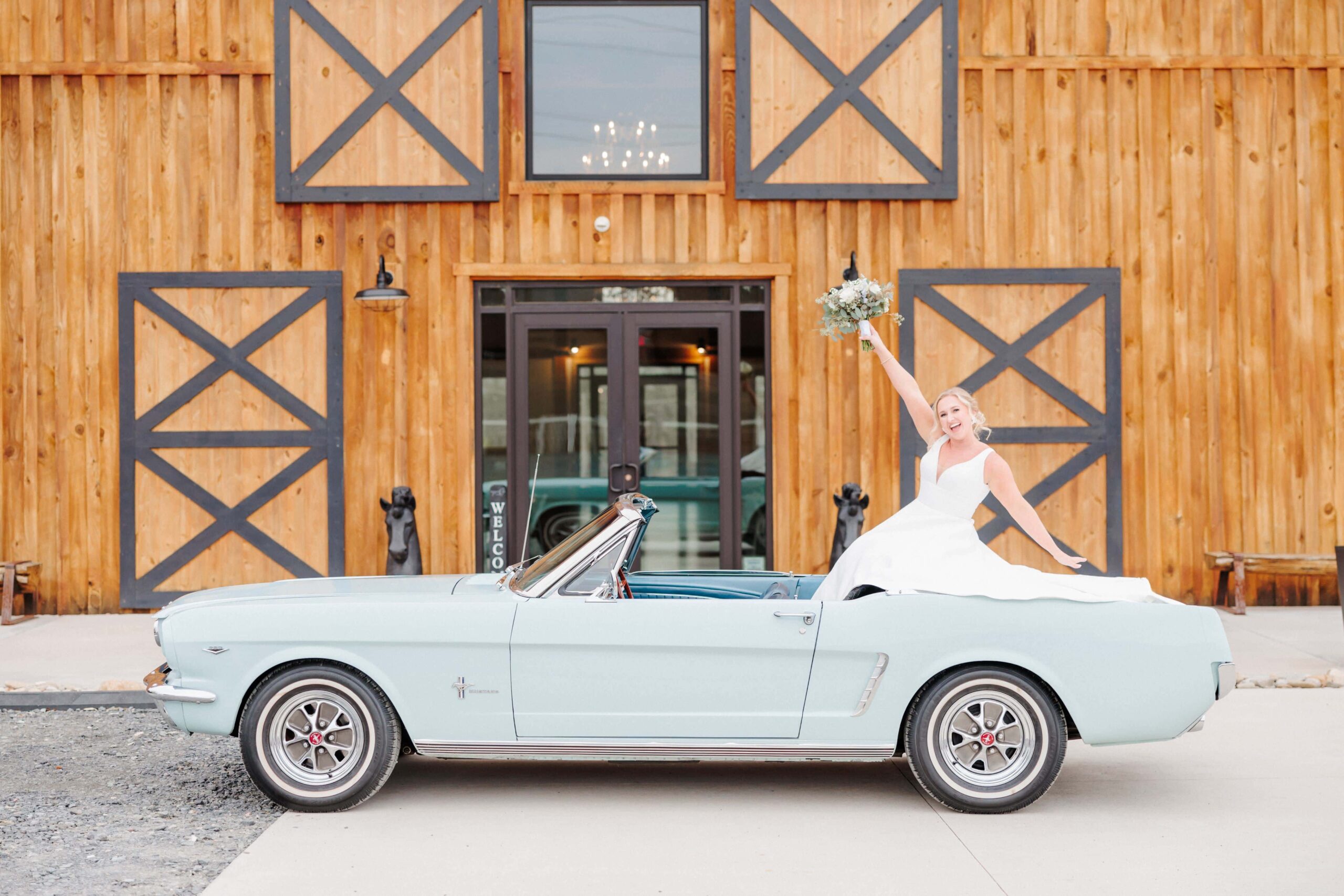 The bride cheers from the back seat of her classic car, throwing her bouquet of flowers up.