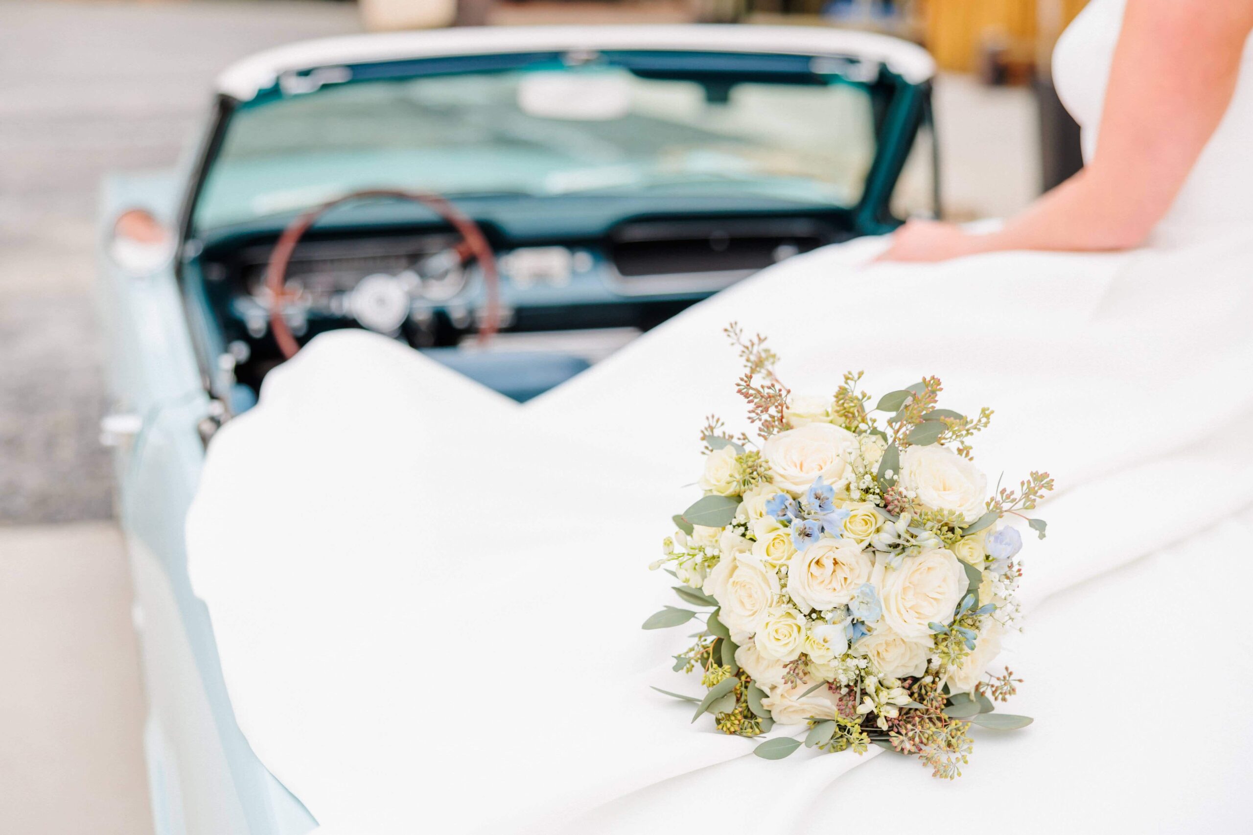 A bridal photo of a white and blue bouquet on top of a classic car.