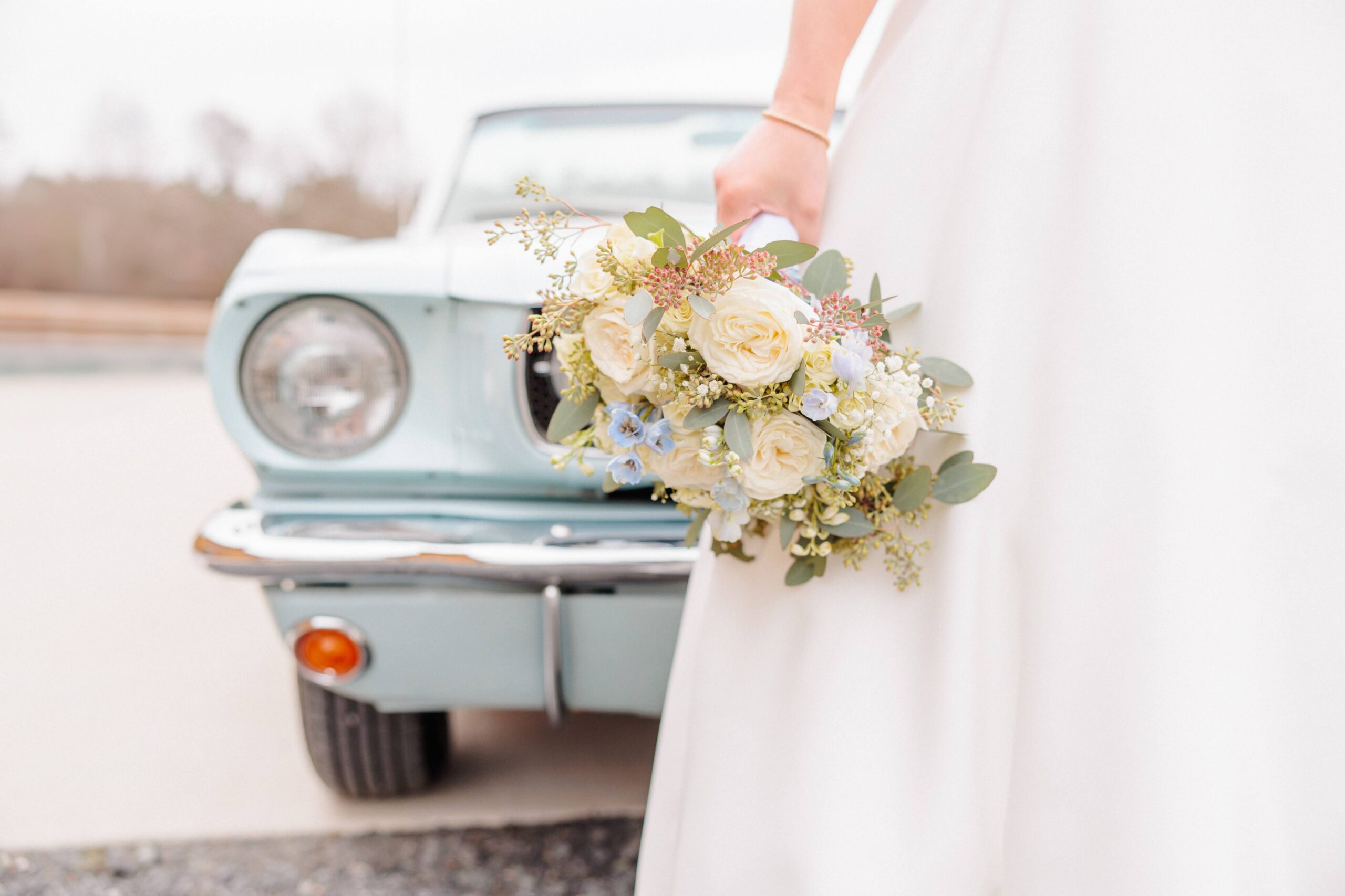 A bridal bouquet can be seen in front of the headlights of this vintage classic car.