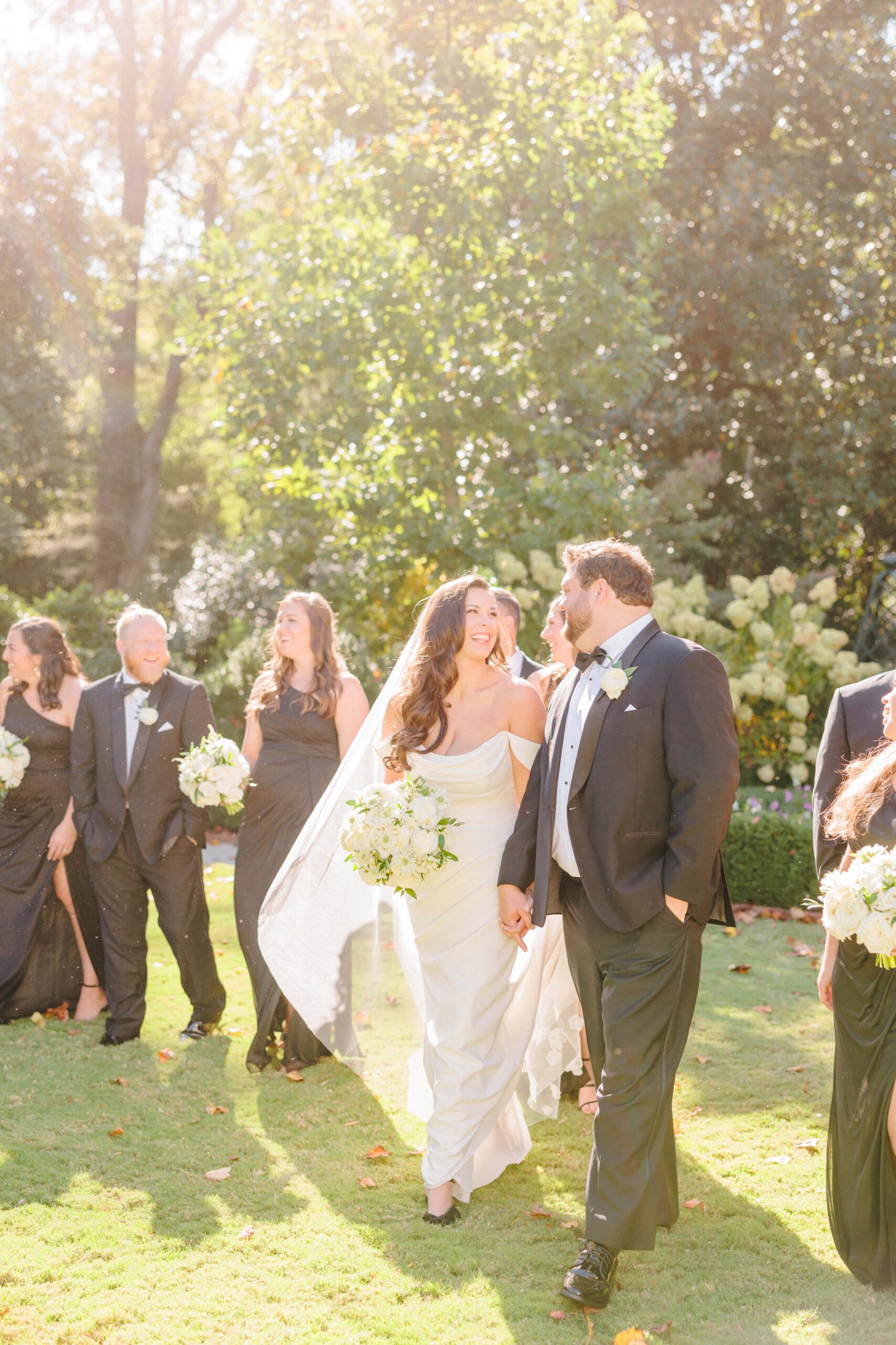 The bride and groom walk with their bridal party on the Duke Mansion lawn as they pose for their wedding photos.