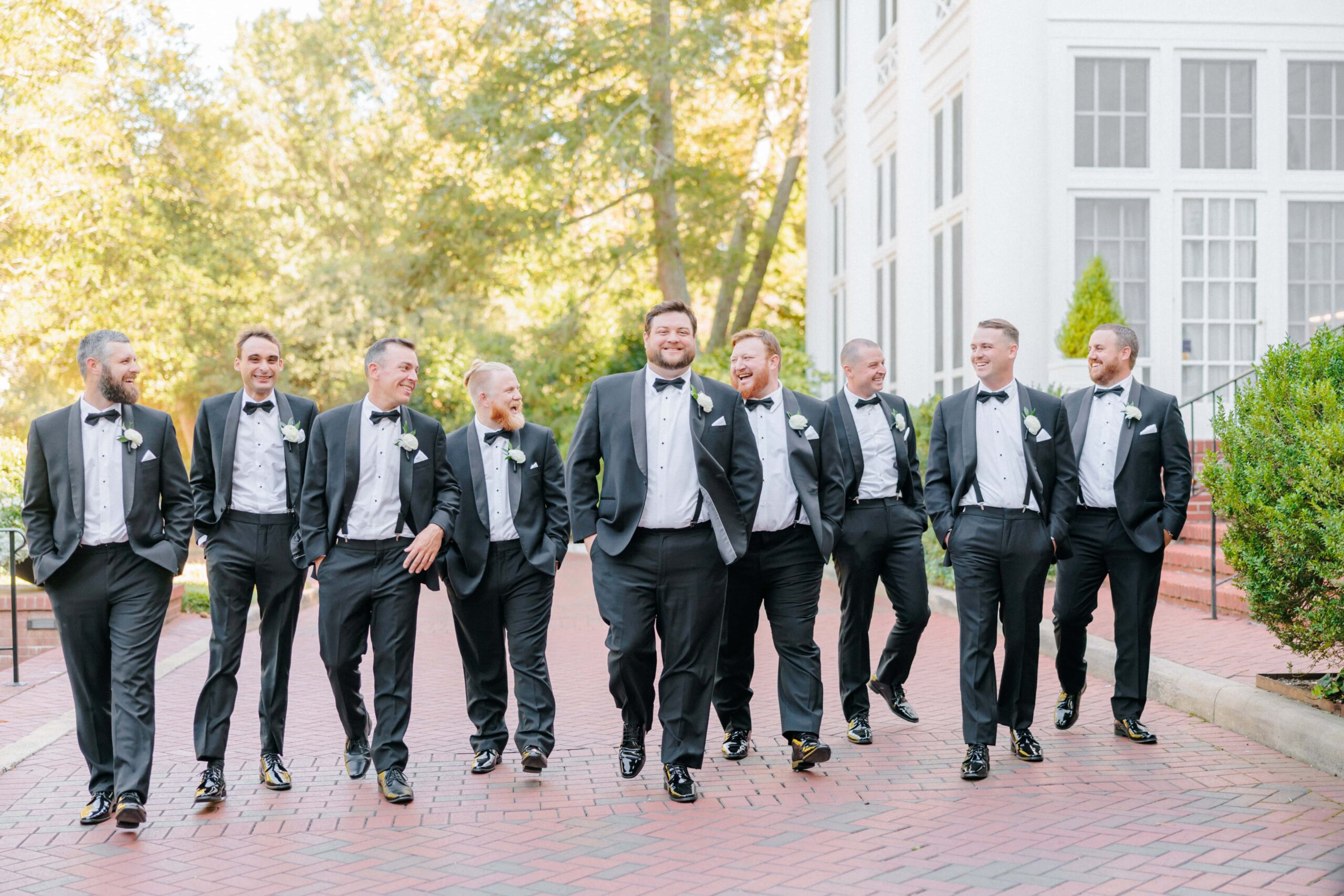 The groom and his groomsmen laugh and walk in front of the Duke Mansion.