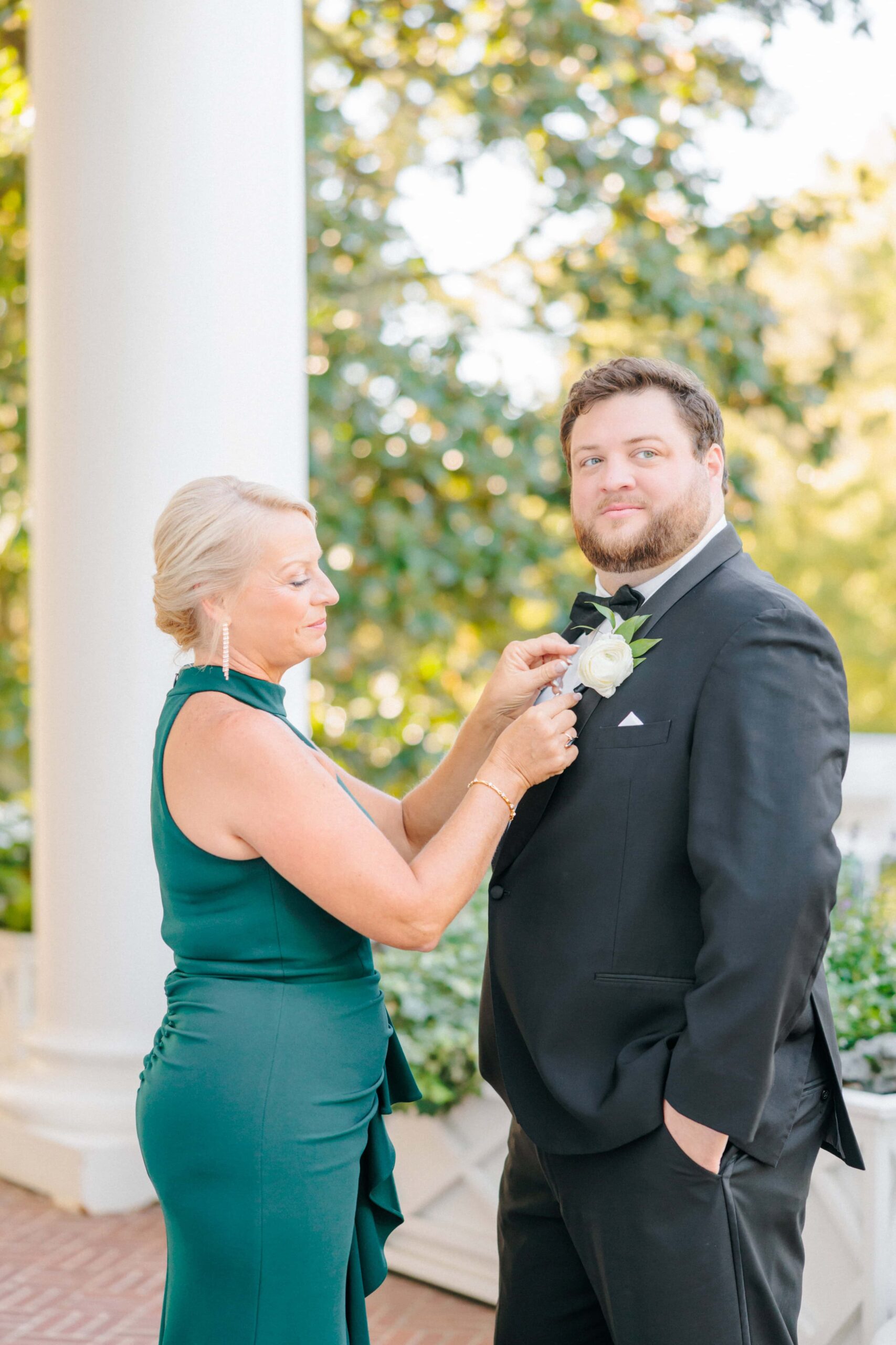 The groom finishes getting ready for his wedding photos with his mom on the steps of the Duke Mansion.